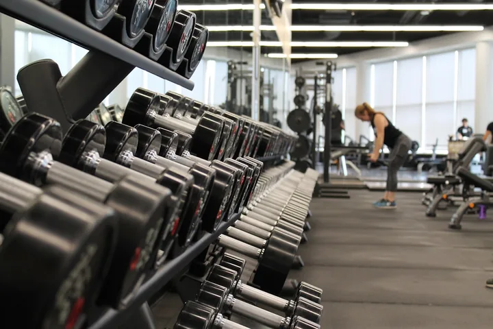 A rack of dumbbells in a gym, someone training in the background